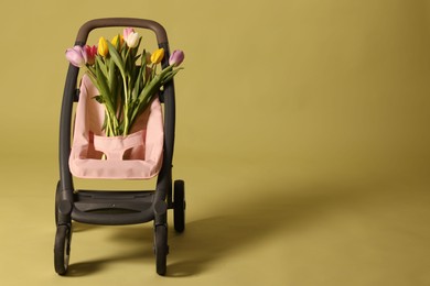 Photo of Stylish doll stroller and tulips on olive background, space for text. Kid's toy