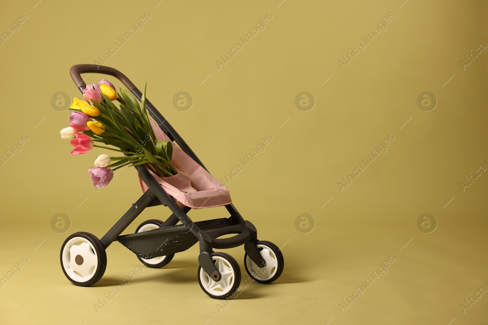 Photo of Stylish doll stroller and tulips on olive background, space for text. Kid's toy