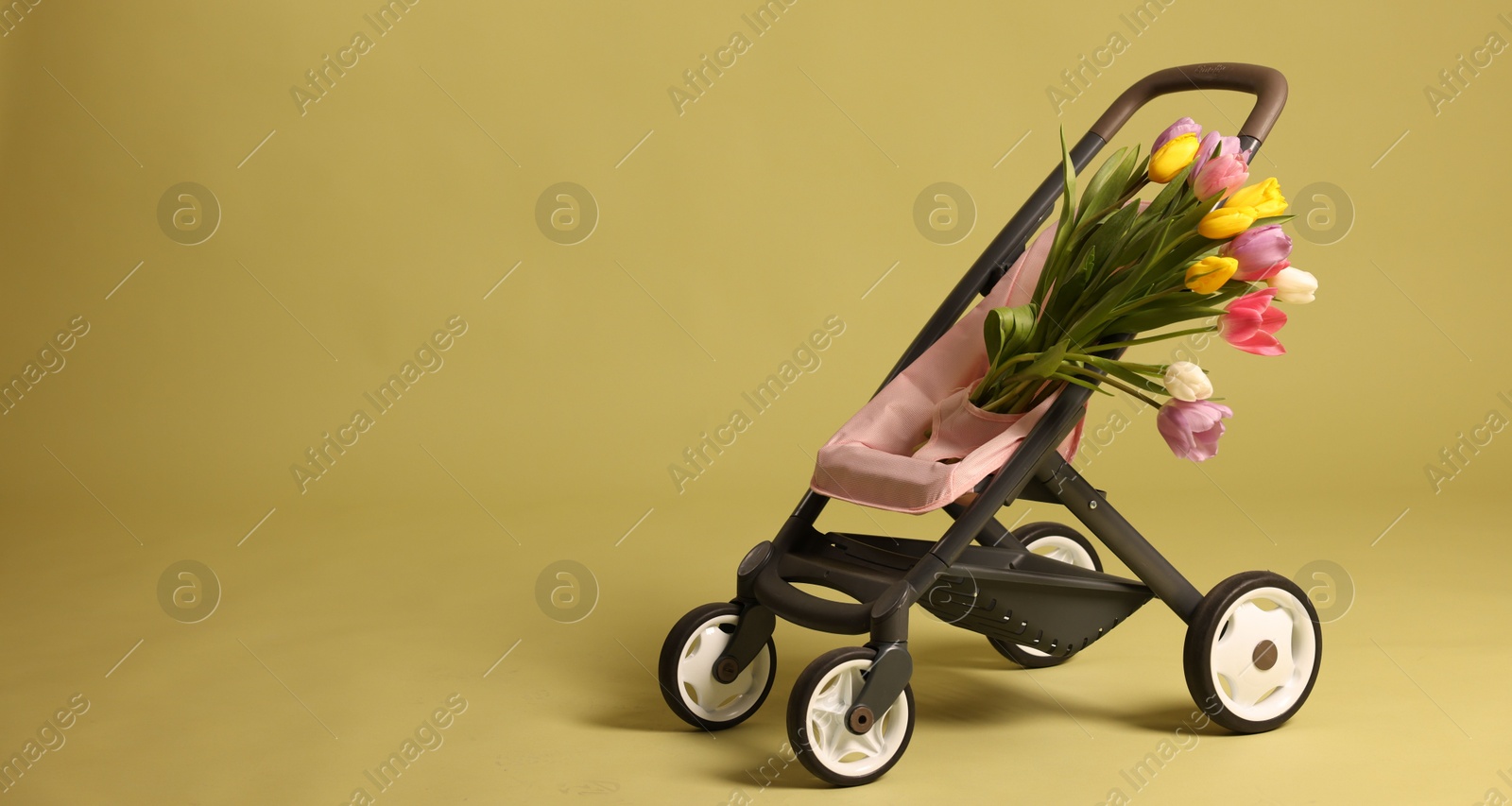 Photo of Stylish doll stroller and tulips on olive background, space for text. Kid's toy