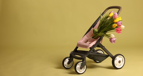 Photo of Stylish doll stroller and tulips on olive background, space for text. Kid's toy