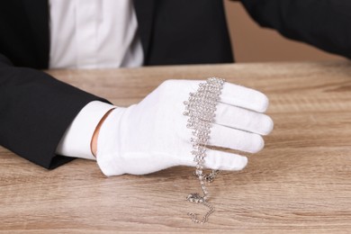 Photo of Appraiser in gloves with luxury necklace at wooden table, closeup