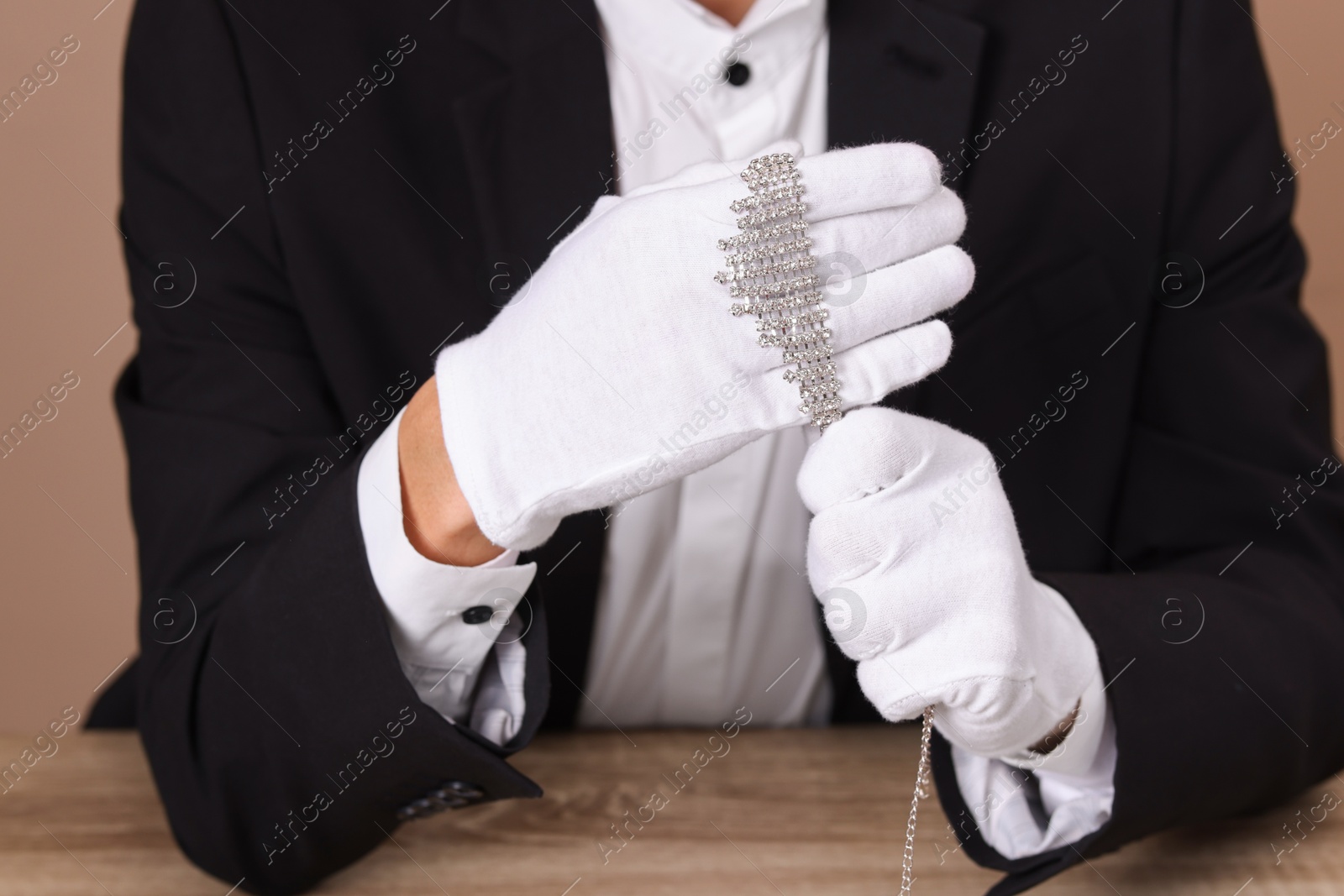 Photo of Appraiser in gloves with luxury necklace at wooden table, closeup