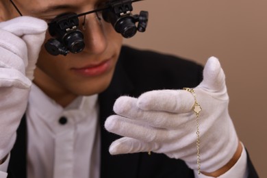 Photo of Appraiser evaluating luxury jewelry on brown background, closeup