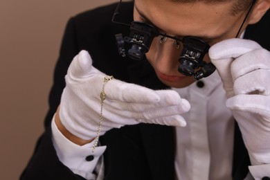 Photo of Appraiser evaluating luxury jewelry on brown background, closeup