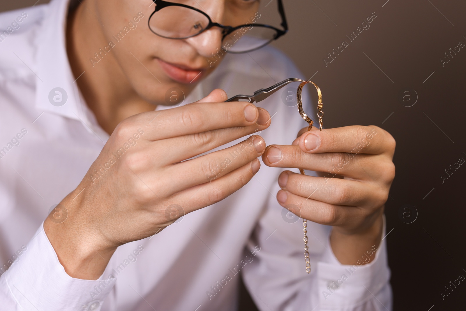 Photo of Appraiser with tweezers evaluating luxury jewelry on brown background, closeup