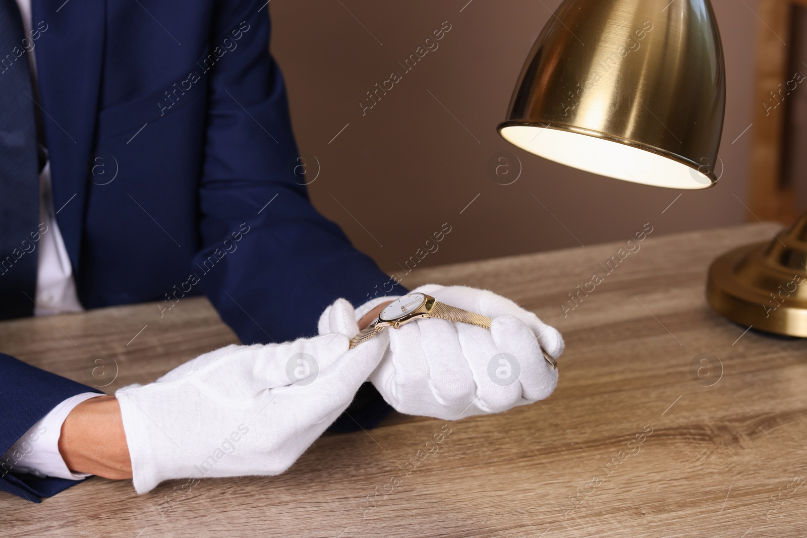 Photo of Appraiser with luxury wristwatch at wooden table, closeup