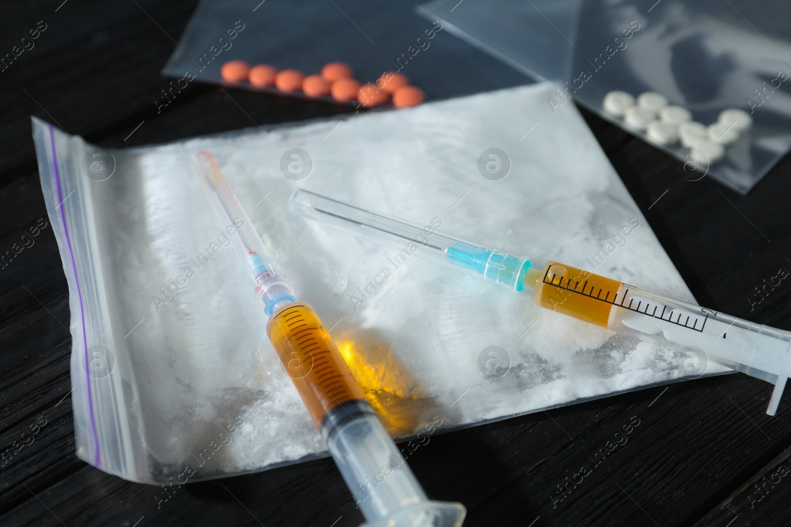 Photo of Drug addiction. Plastic bag with powder, syringes and pills on black wooden table, closeup