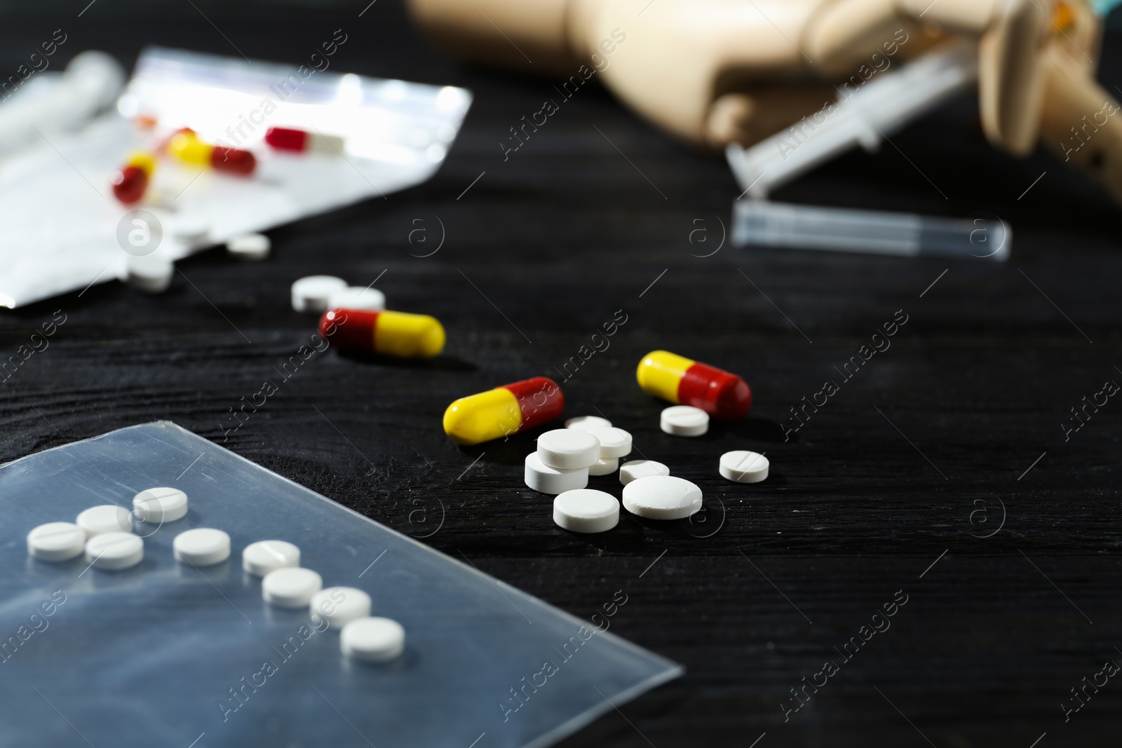 Photo of Drug addiction. Plastic bag with pills on black wooden table, closeup