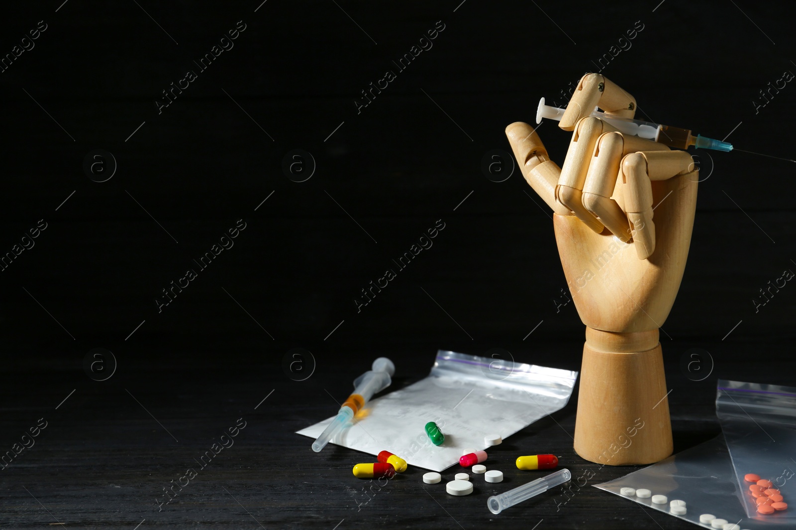 Photo of Drug addiction. Mannequin hand with syringe and pills on black wooden table against dark background, space for text