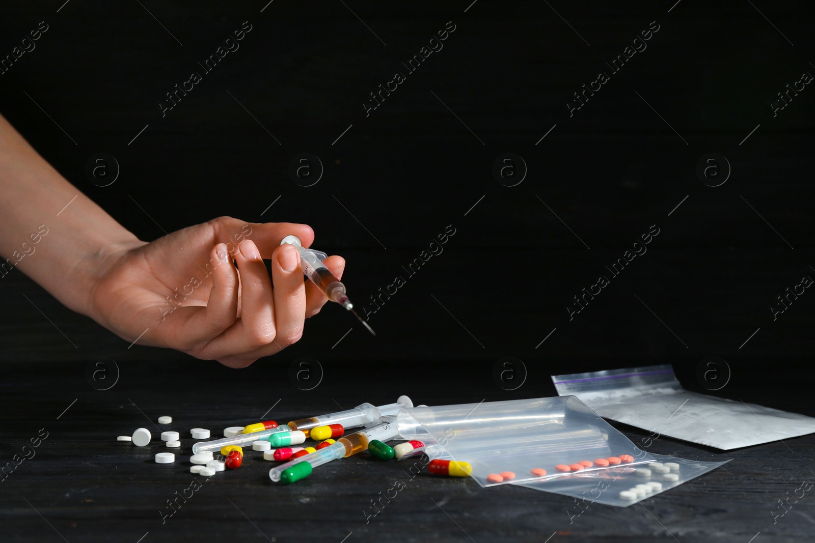 Photo of Drug addiction. Woman with syringe at black wooden table against dark background, closeup. Space for text