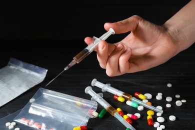 Photo of Drug addiction. Woman with syringe at black wooden table against dark background, closeup