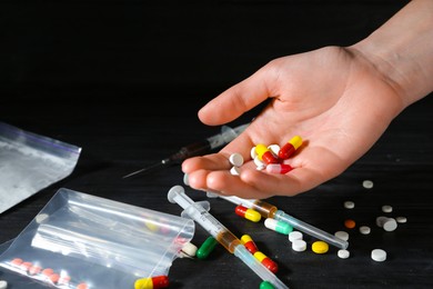 Photo of Drug addiction. Woman with pills at black wooden table, closeup