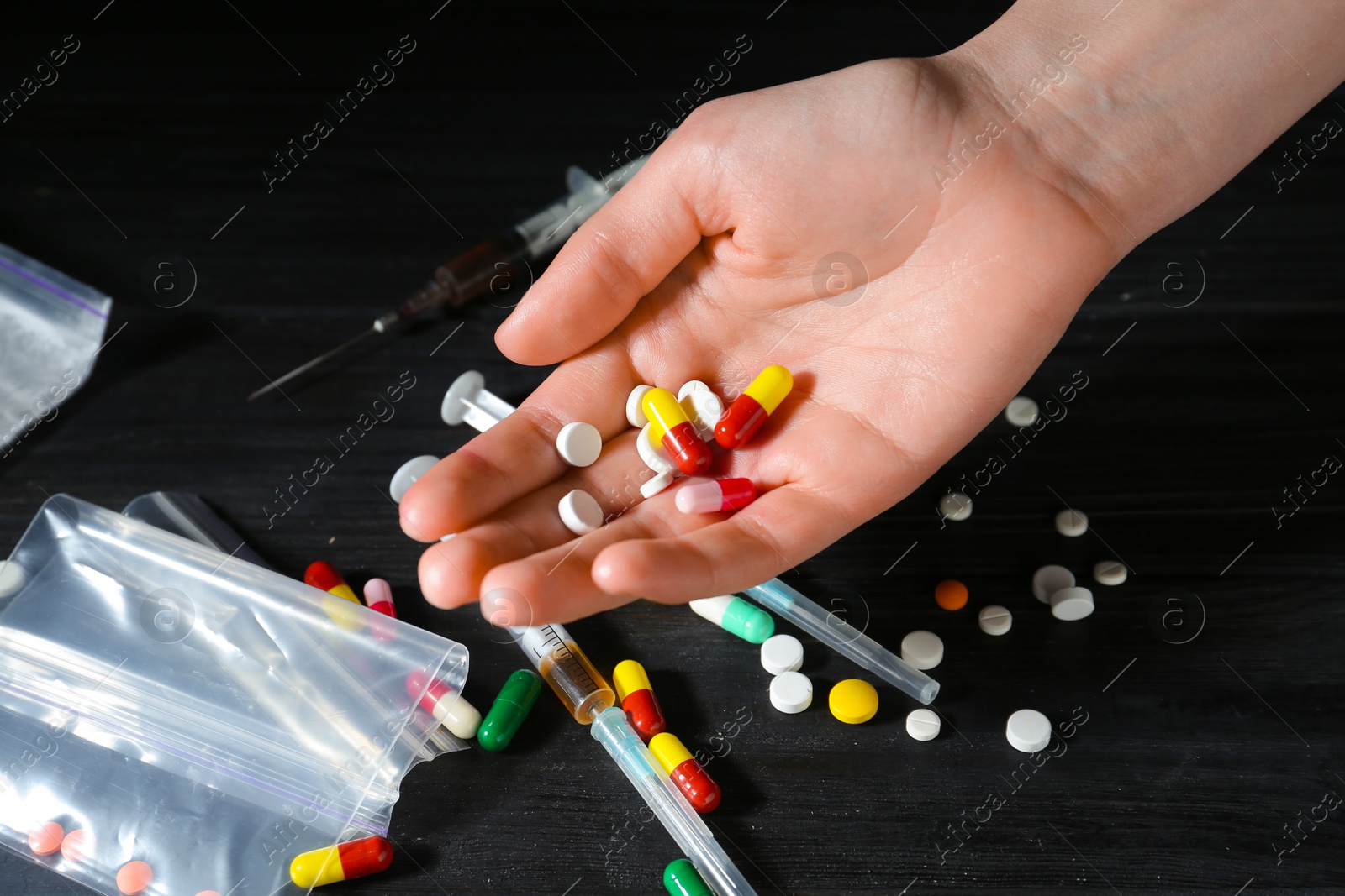 Photo of Drug addiction. Woman with pills at black wooden table, closeup