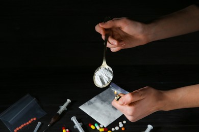 Photo of Drug addiction. Woman lighting spoon with powder against dark background, closeup