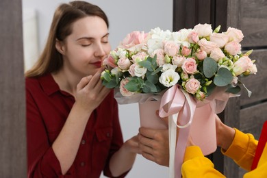 Photo of Woman smelling beautiful flowers from delivery man at door