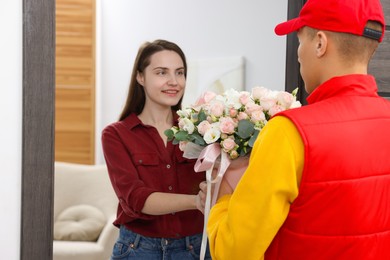 Photo of Happy woman receiving gift box with beautiful floral composition from delivery man at door