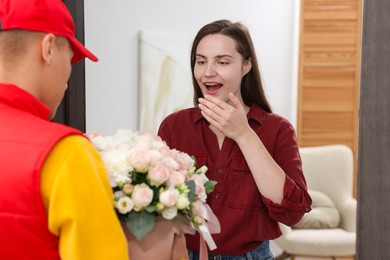 Photo of Delivery man giving gift box with beautiful floral composition to surprised woman at door