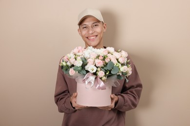 Photo of Smiling delivery man holding gift box with beautiful floral composition on beige background