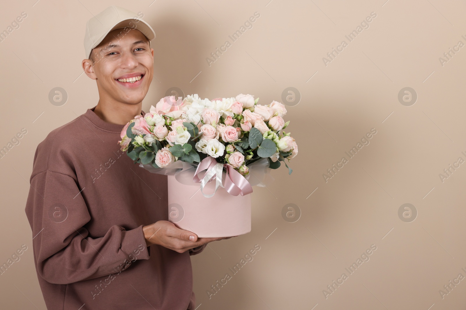 Photo of Smiling delivery man holding gift box with beautiful floral composition on beige background. Space for text