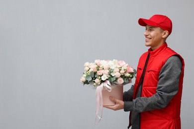 Photo of Smiling delivery man holding gift box with beautiful floral composition on grey background. Space for text