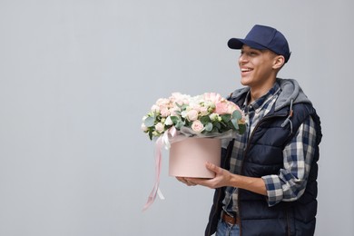 Photo of Smiling delivery man holding gift box with beautiful floral composition on grey background. Space for text