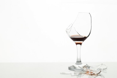 Photo of Pieces of broken glass with wine on table against white background, space for text