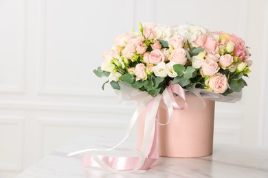 Photo of Gift box with bouquet of beautiful flowers and eucalyptus branches on marble table against white wall. Space for text