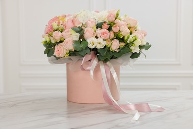 Photo of Gift box with bouquet of beautiful flowers and eucalyptus branches on marble table against white wall