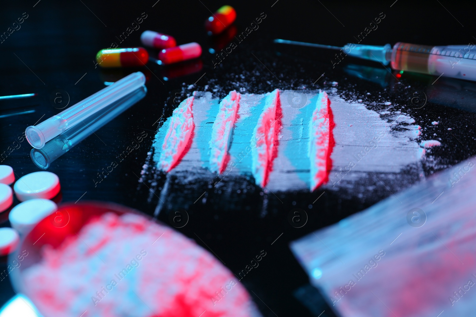 Photo of Drug addiction. Powder, pills and syringe on black table in neon lights, closeup