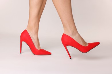 Photo of Woman wearing beautiful red high heeled shoes on white background, closeup