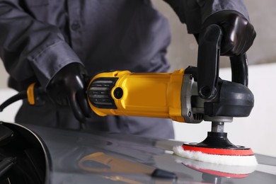 Photo of Man polishing car hood with orbital polisher indoors, closeup