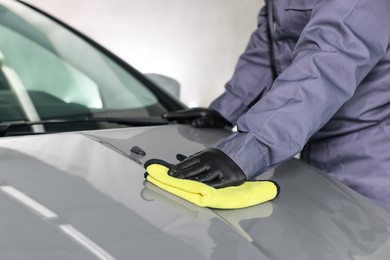 Photo of Man polishing car hood with rag indoors, closeup