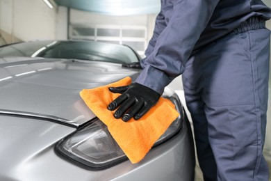 Photo of Man polishing car headlight with orange rag indoors, closeup