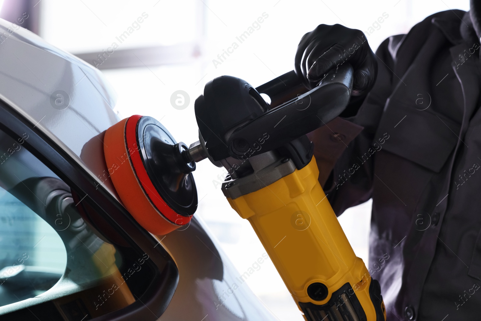 Photo of Man polishing car with orbital polisher indoors, closeup