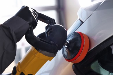 Photo of Man polishing car with orbital polisher indoors, closeup