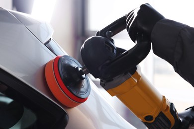 Photo of Man polishing car with orbital polisher indoors, closeup