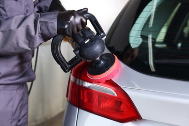 Photo of Man polishing car rear light with orbital polisher indoors, closeup