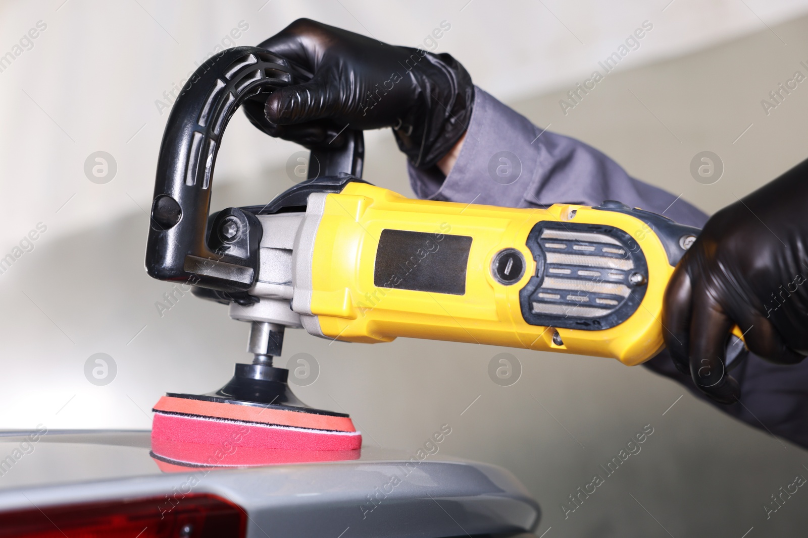 Photo of Man polishing car with orbital polisher indoors, closeup