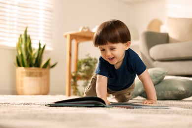 Photo of Cute little boy with book on floor at home, space for text