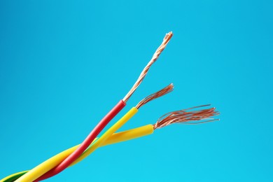 Photo of Stripped electrical wires with copper strands on light blue background, closeup