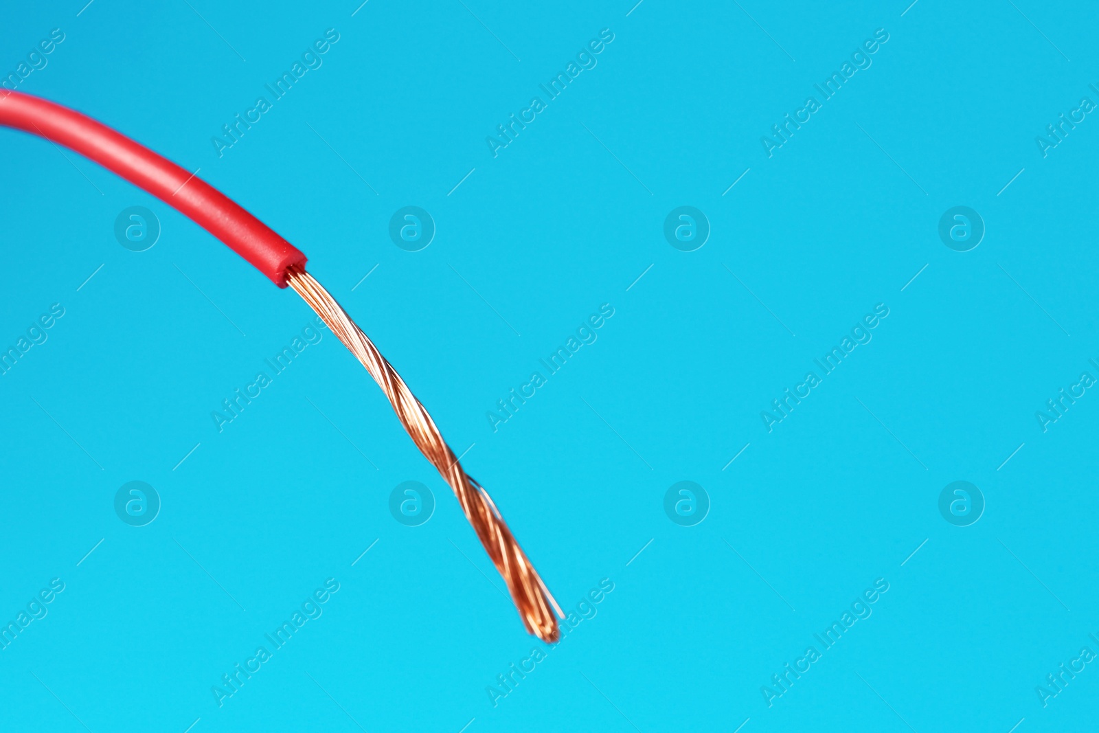 Photo of Stripped electrical wire with copper strands on light blue background, closeup