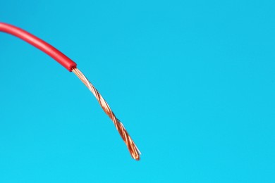 Photo of Stripped electrical wire with copper strands on light blue background, closeup