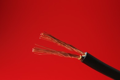 Photo of Stripped electrical wire with copper strands on red background, closeup