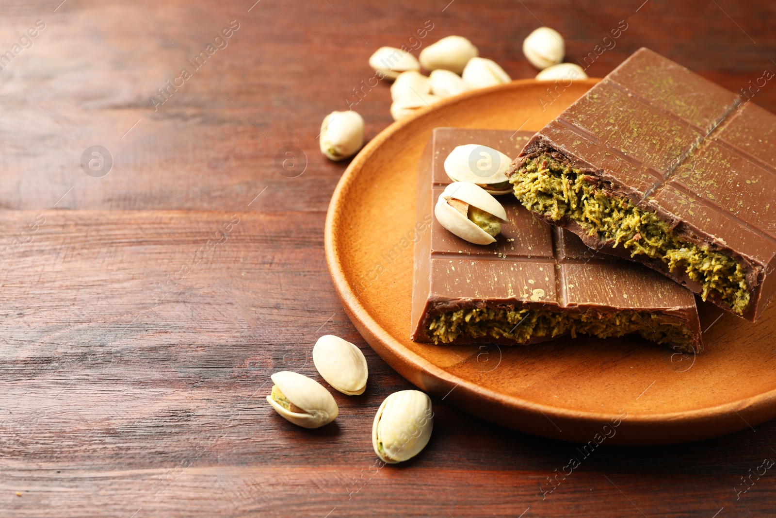 Photo of Pieces of tasty Dubai chocolate with pistachios and knafeh on wooden table, closeup. Space for text