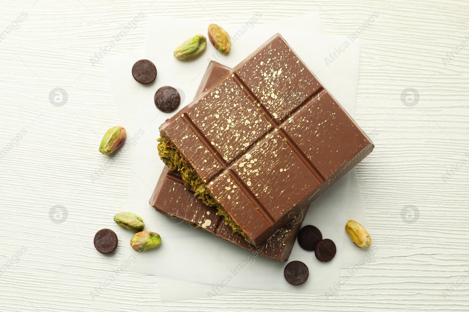 Photo of Pieces of tasty Dubai chocolate with pistachios, knafeh and cacao chips on white wooden table, flat lay