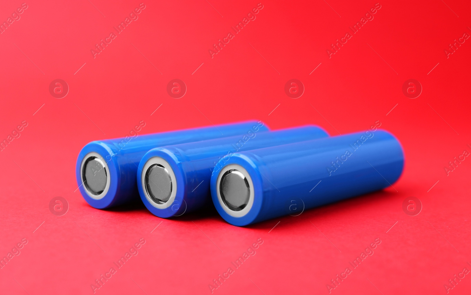 Photo of Three AA cell batteries on red background, closeup. Space for text