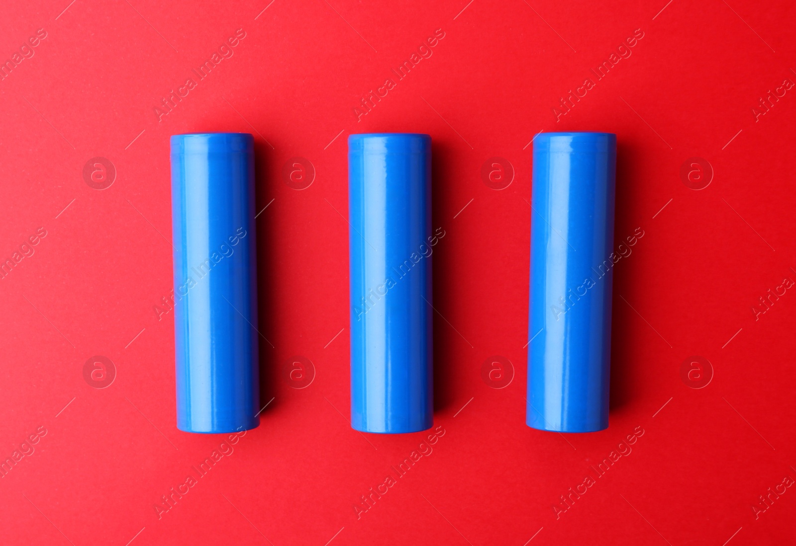 Photo of Three AA cell batteries on red background, top view