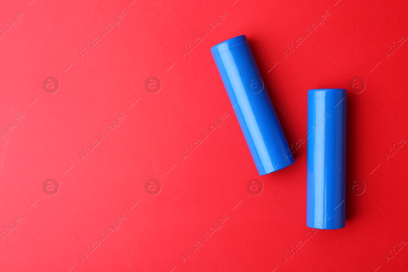 Photo of Two AA cell batteries on red background, top view. Space for text