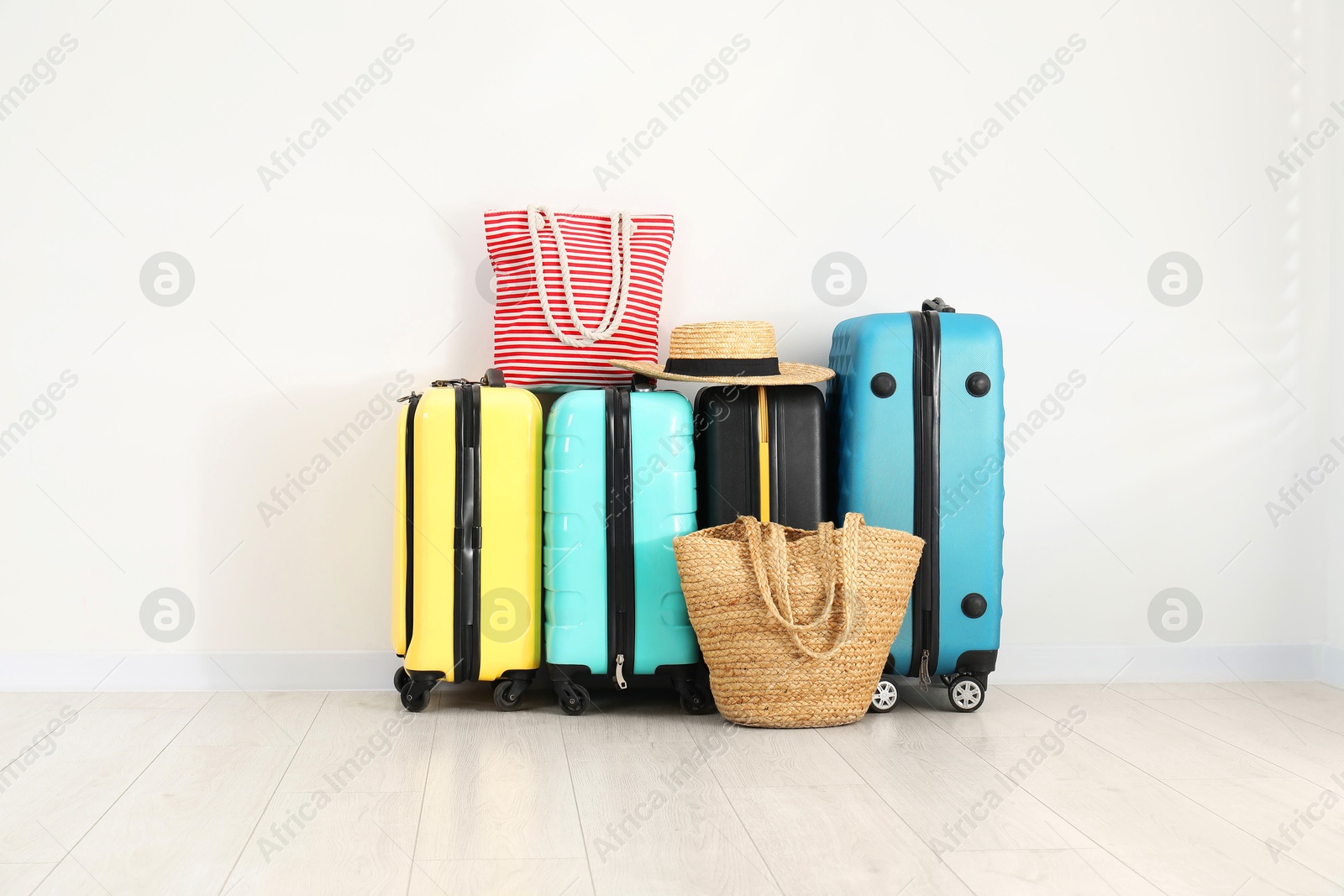 Photo of Colorful suitcases, beach bags and straw hat on floor near white wall