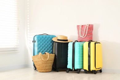 Photo of Colorful suitcases, beach bags and straw hat on floor near white wall